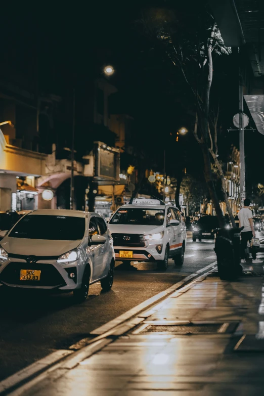 a busy street with parked cars on both sides and the street lights on both