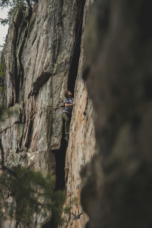 a man climbing up the side of a mountain next to trees