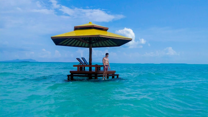 a man standing in the ocean next to an umbrella