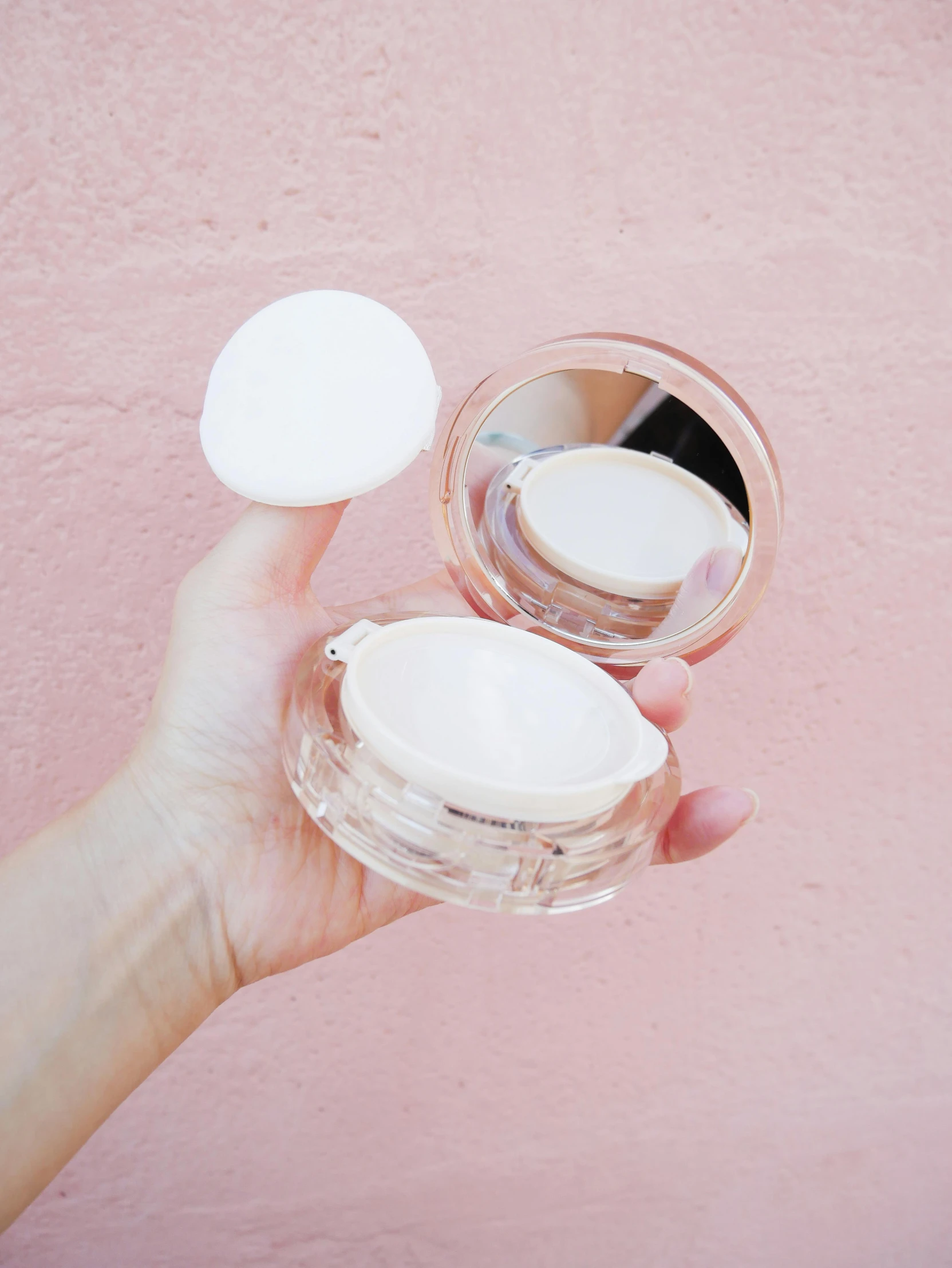 a woman holding a jar of compact powder in her left hand and another powder in the other hand