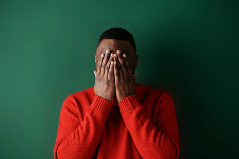 man in red sweater covering his eyes with both hands