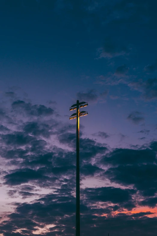 a lamp post in the middle of a sunset with the sky behind it