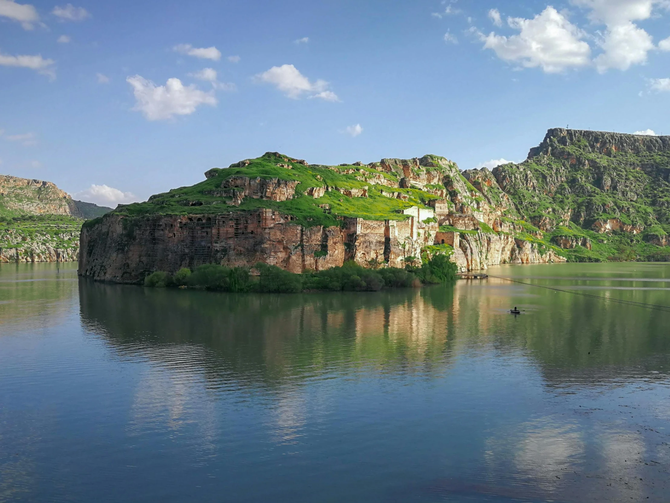 small island surrounded by a rocky cliff sits on still water