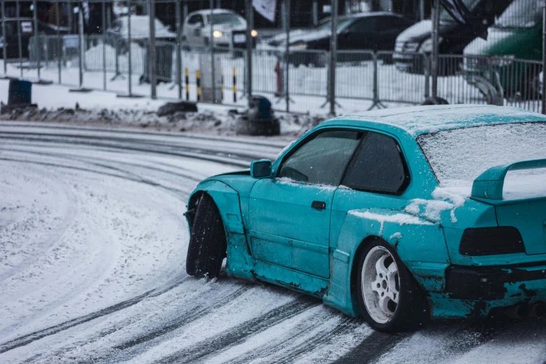 a blue car driving down a street covered in snow
