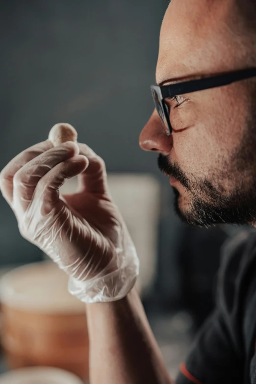 a man with eyeglasses and gloves holds a piece of food