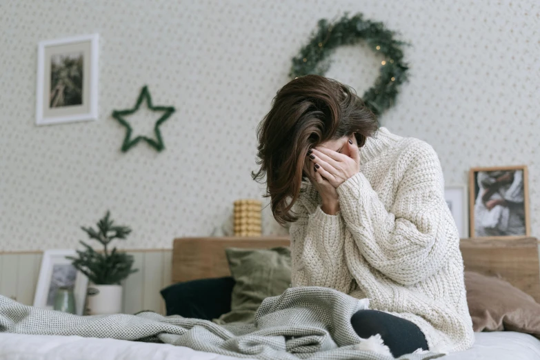 a woman covering her face with her hands sitting on the edge of a bed