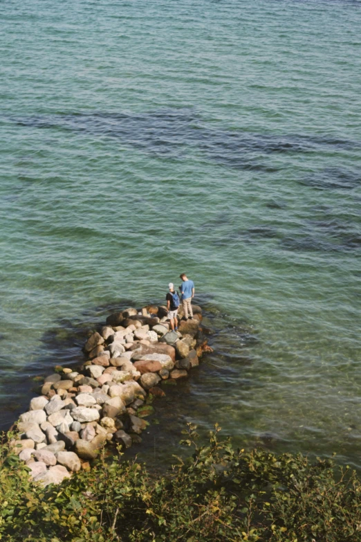 a man and woman walking on a rock formation at the edge of water