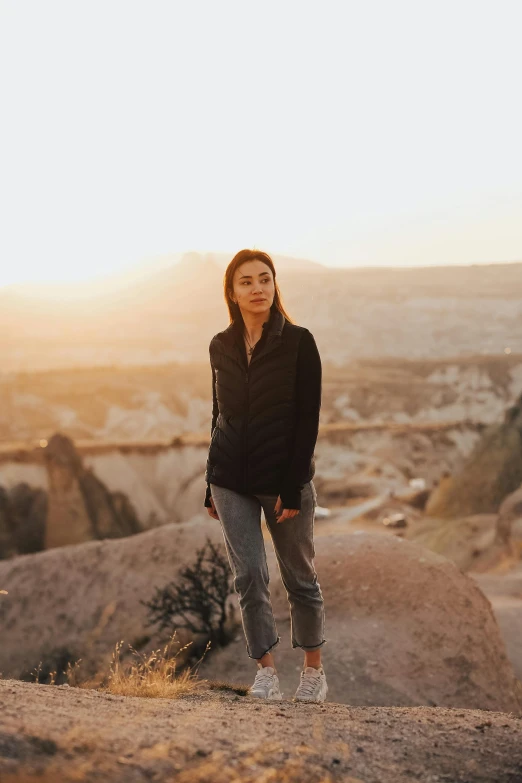 a woman is standing on a rocky hill overlooking the landscape