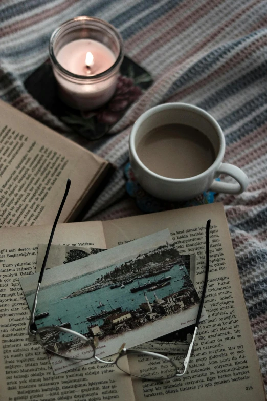 an open book with eye glasses next to a glass of liquid