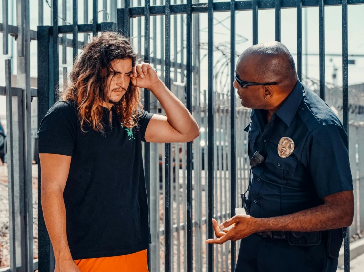 two men stand together next to a fence while one looks down at the other