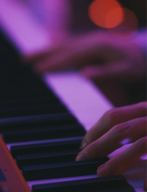 someones hands playing on a piano with pink lights in the background