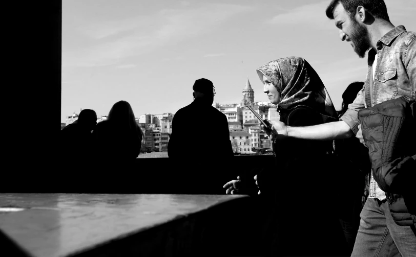 a woman looking at her cellphone while a man and a woman are standing in a line