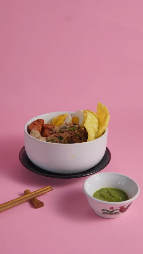 a white bowl with chips, beef and guacamole next to some dipping sauce