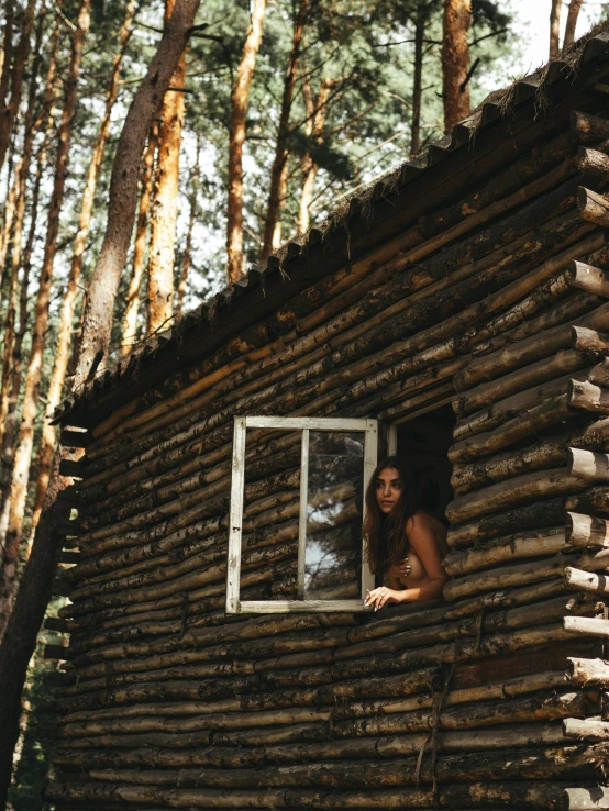 a woman leaning up against a log cabin window