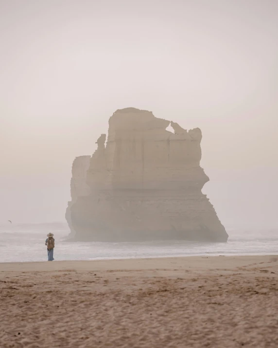 a person on the beach looking at a rock formation