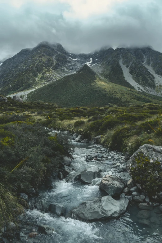 stream flowing between grass and rocks with mountains in background