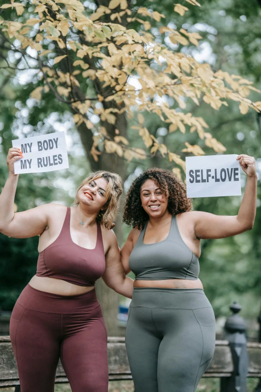 two women wearing tights hold signs in front of trees