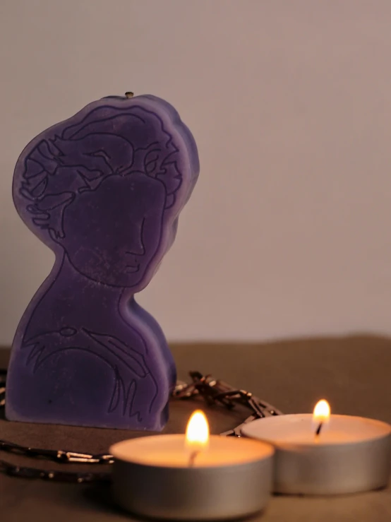 two candles sitting next to a little wax block with a face on it