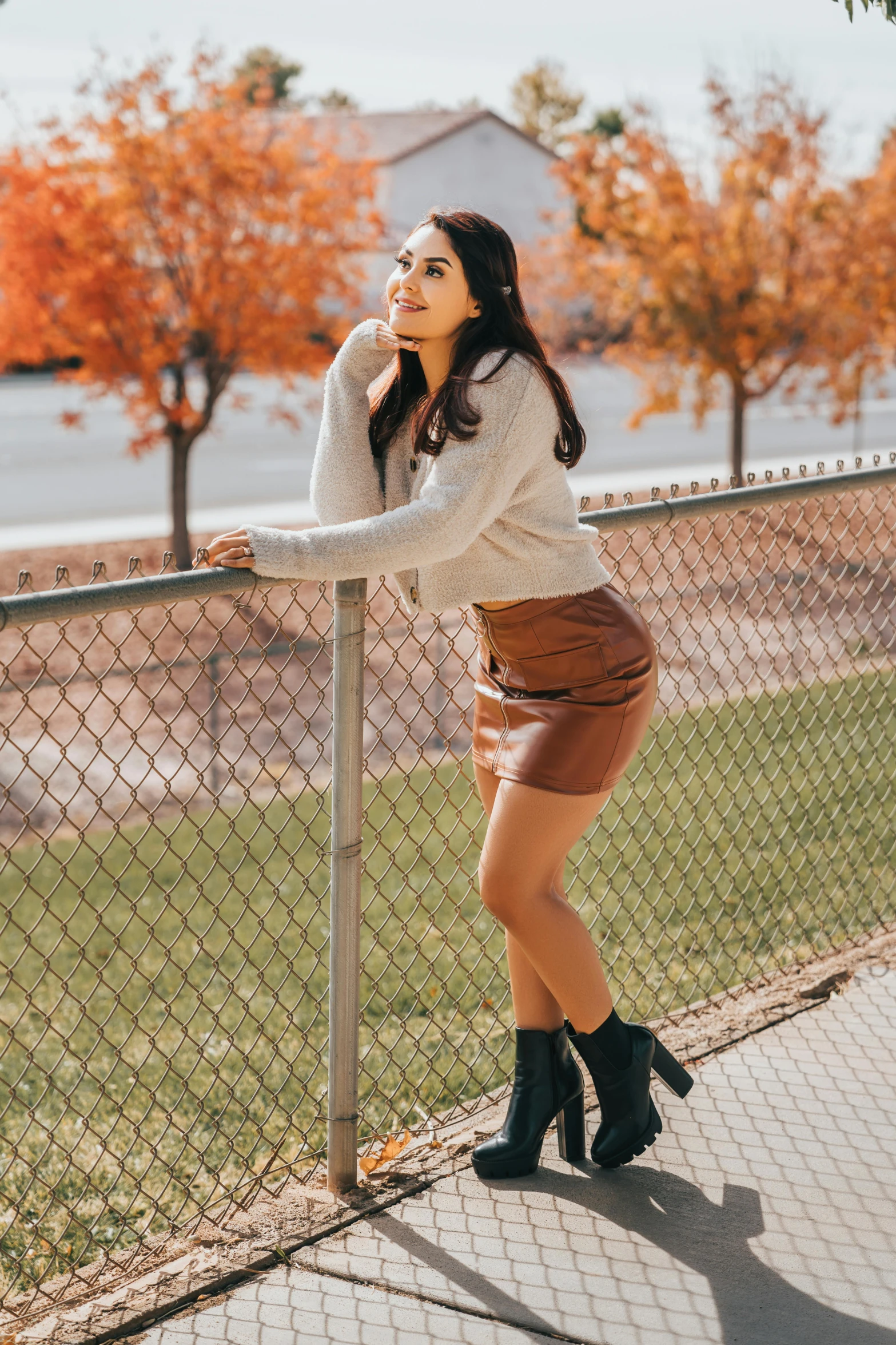 a woman wearing black boots posing near a fence