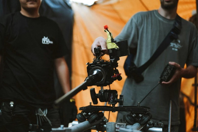 two men stand behind an orange backdrop with a camera attached to it