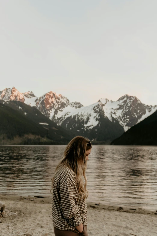 a woman standing in front of a lake with mountains in the background