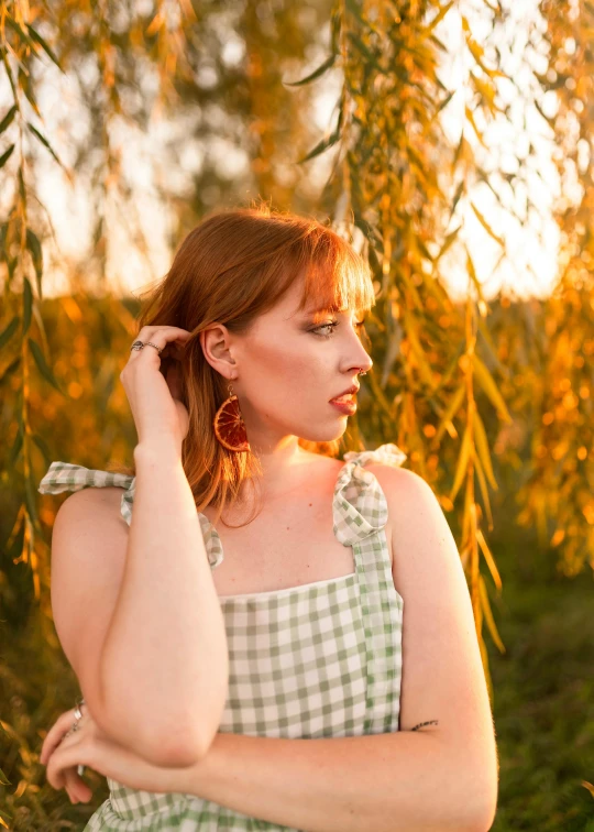 a woman in gingham poses near a tree with her hair pulled up