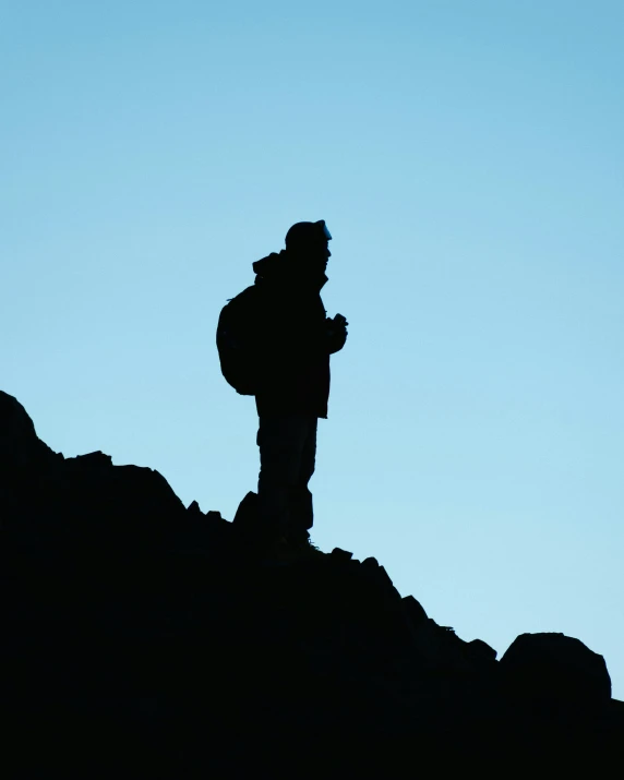 a man stands on a hill, with his arms crossed and looking out at the sky