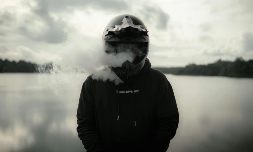 a man in a black jacket wearing a motorcycle helmet standing near a lake