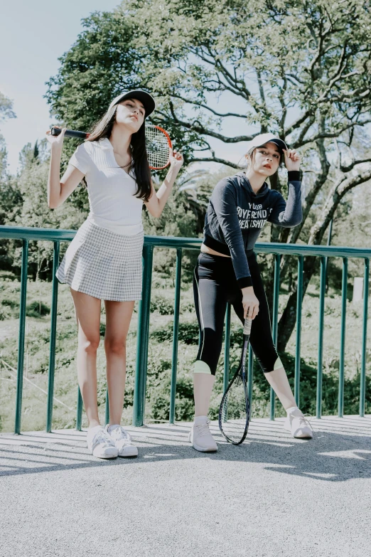 two girls holding tennis racquets and looking at soing on the ground