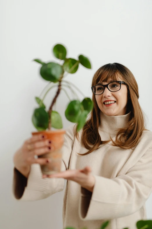 a woman holding up a potted plant with small leaves