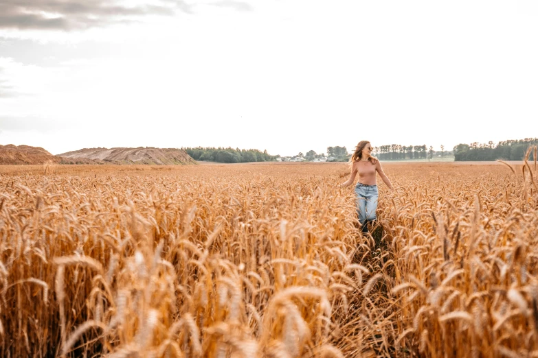 a woman in a blue jeans walking through a field of grass