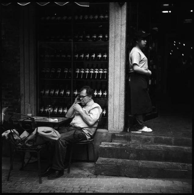 a man sitting in front of a store talking on his phone