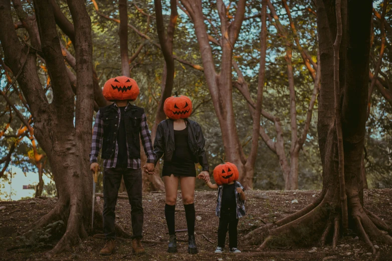 a couple of people walking through a forest with pumpkin hats