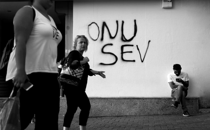 people are outside on the sidewalk with graffiti on the wall