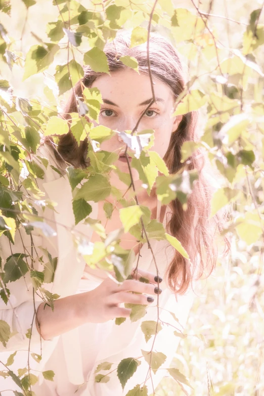 a woman looking through leaves in the sunlight