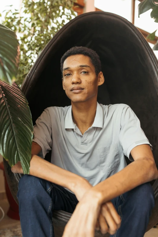 a man with short hair and a grey shirt is sitting in a black chair