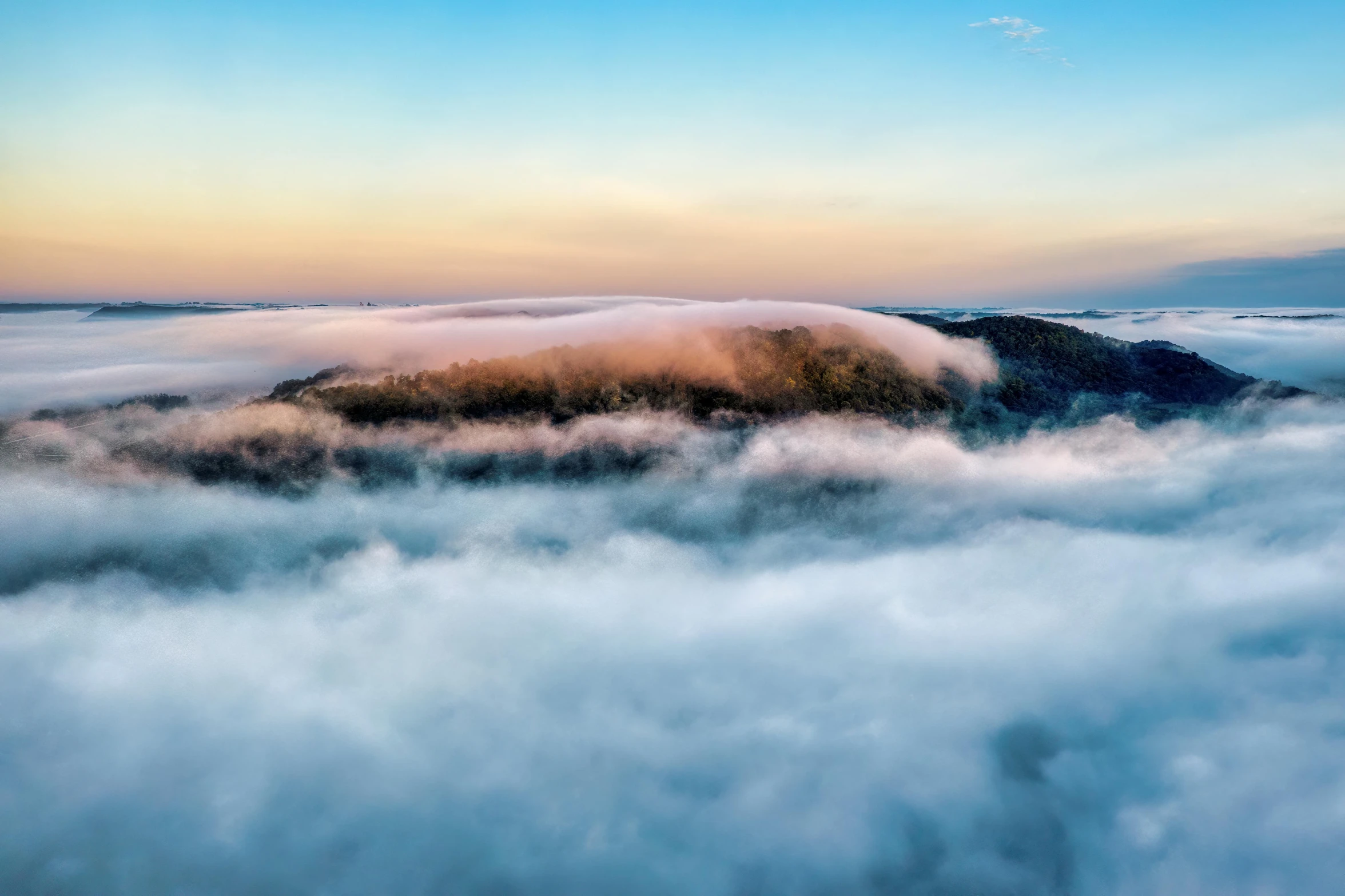 a view of the clouds and a small hill