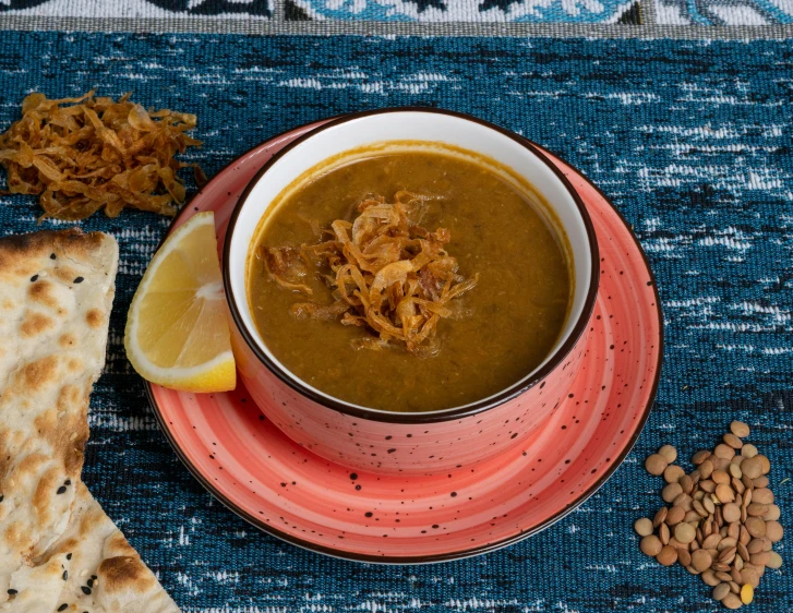 a bowl of soup with a lemon wedge on the side and peanuts nearby