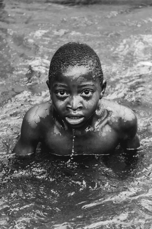 a boy standing in some water and looking at the camera