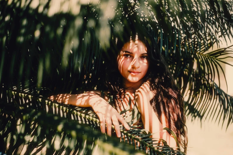 a girl is posing for a picture through a palm tree