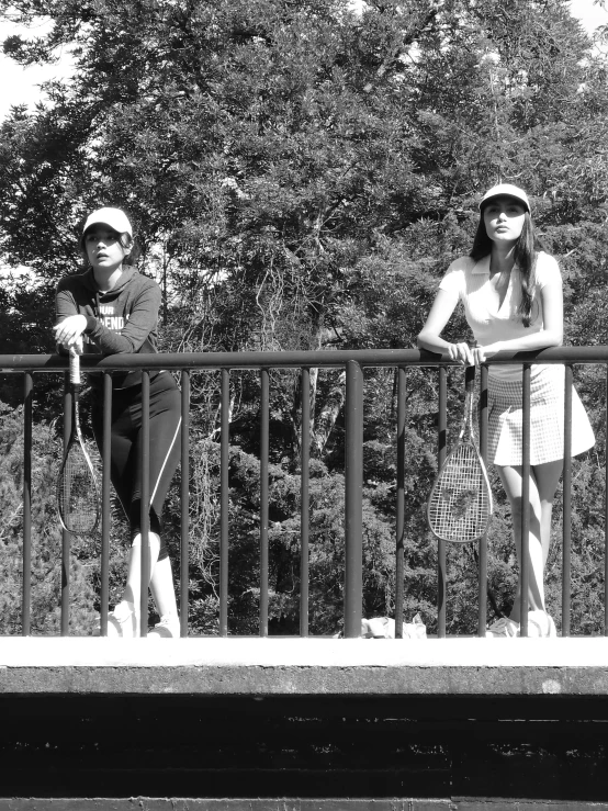 two women holding tennis rackets on top of a railing