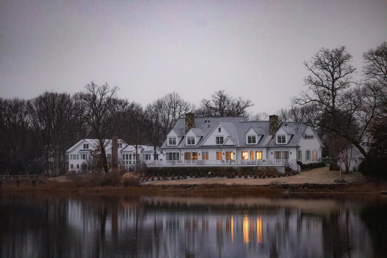 a white house with many windows overlooks a pond at night