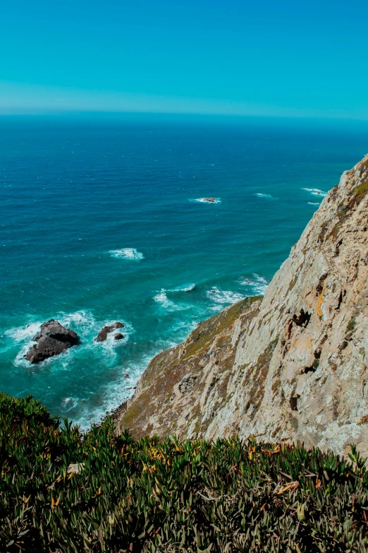 two people sitting on the top of a mountain near the ocean