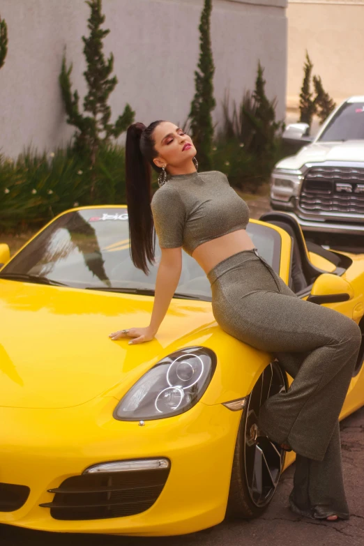 a woman leans against the hood of a yellow sports car