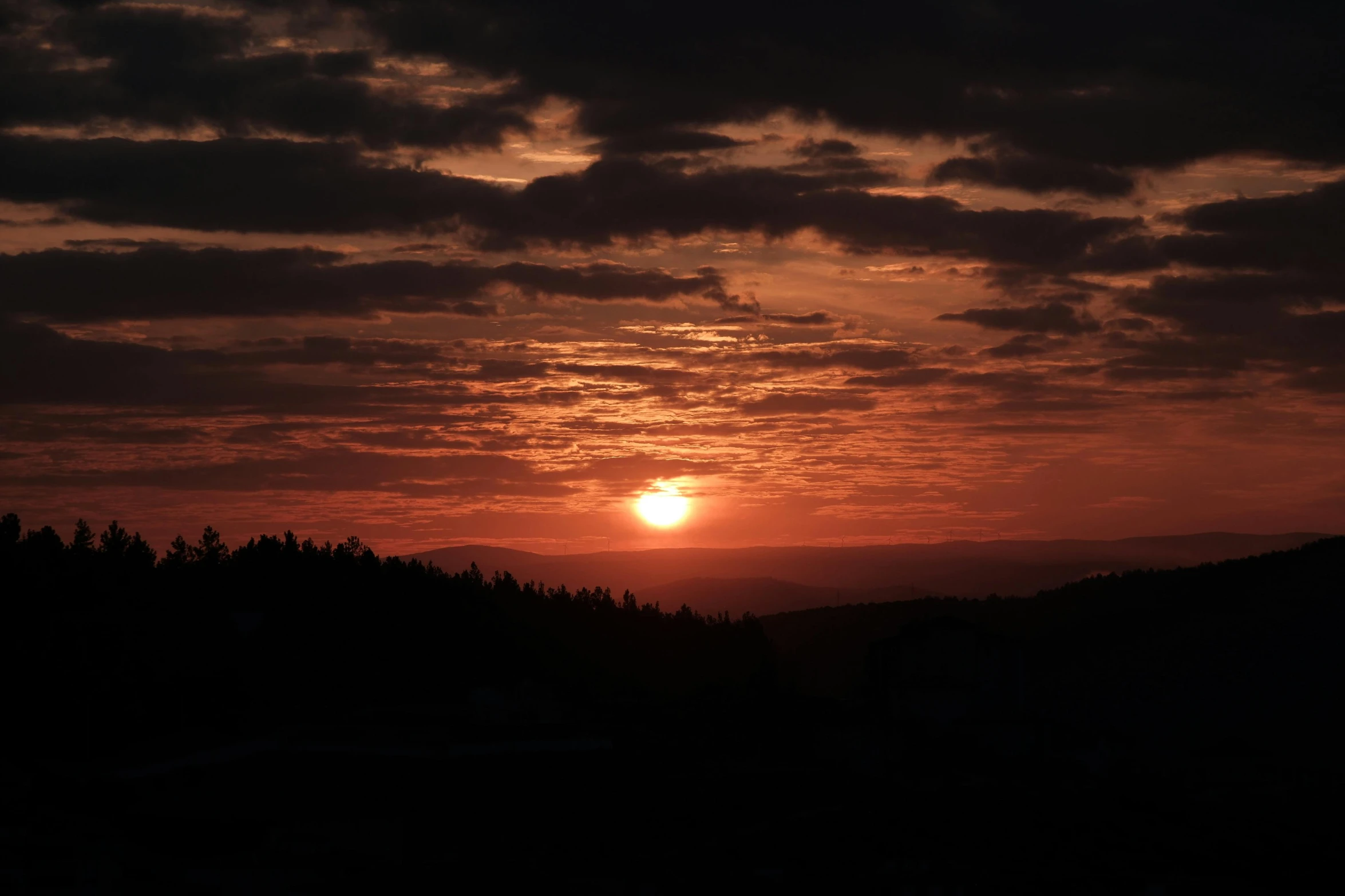 a sun setting over some trees in a mountain