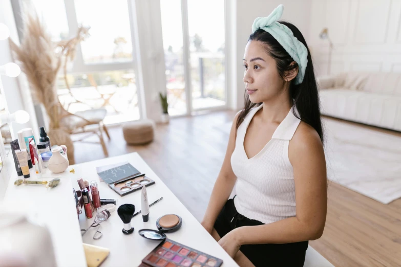 a woman wearing a bow tie is sitting at a table full of makeup and other items