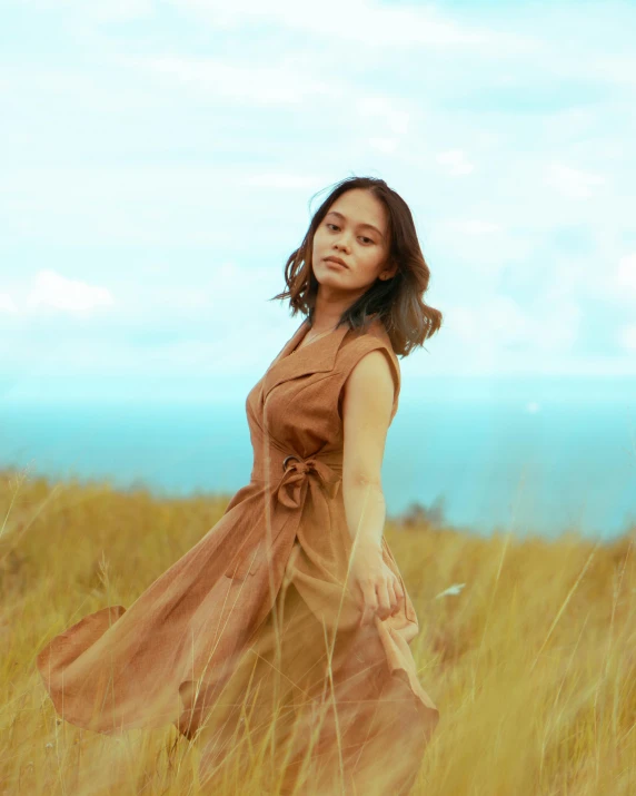 a woman in a field with a brown dress and long brown hair