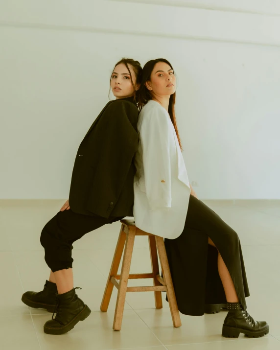 two girls sit on a stool one leaning against the back of another