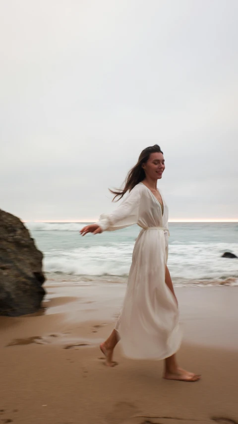 a woman in a white robe running along the shore