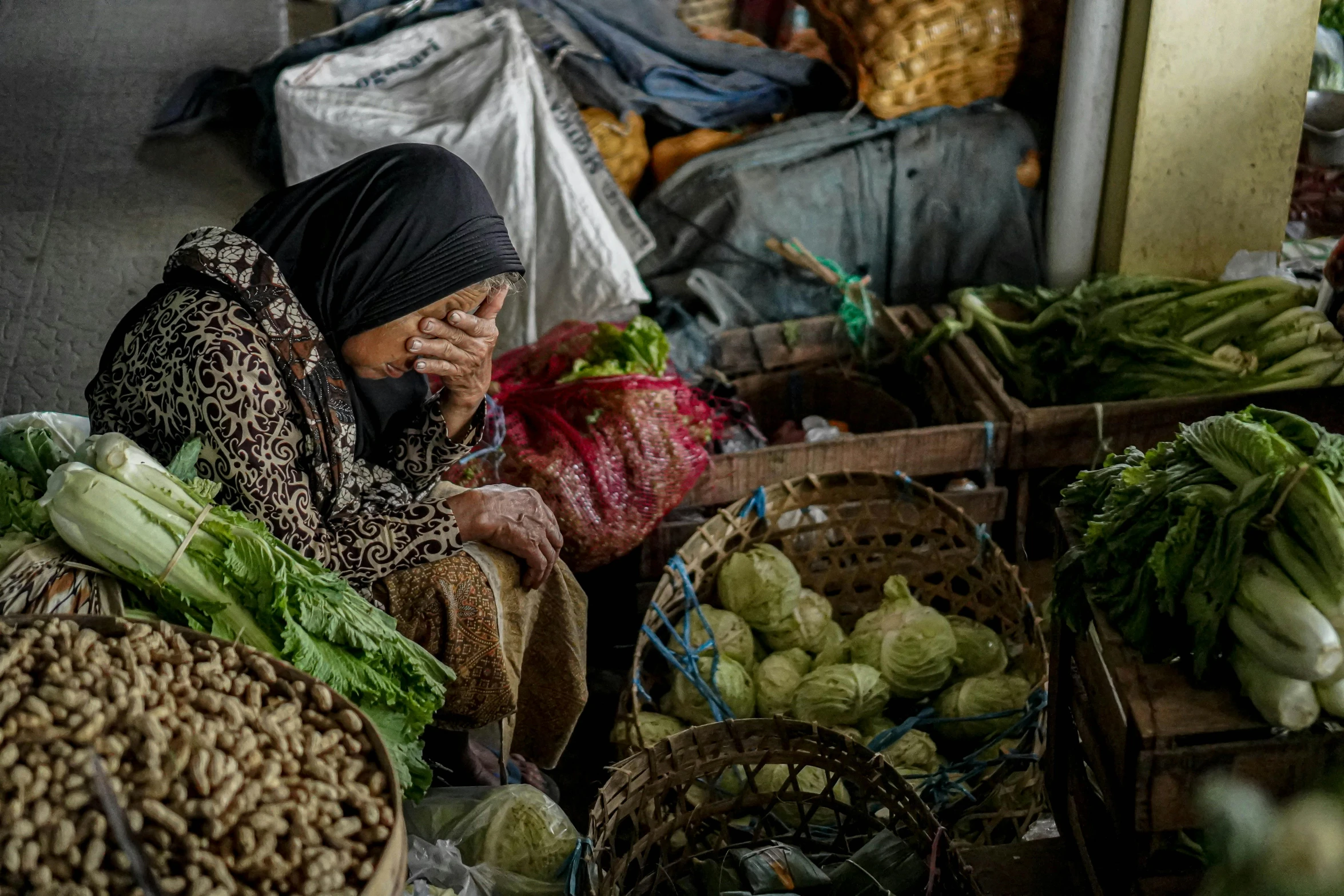 woman in large head scarf sitting next to vegetables and fruits